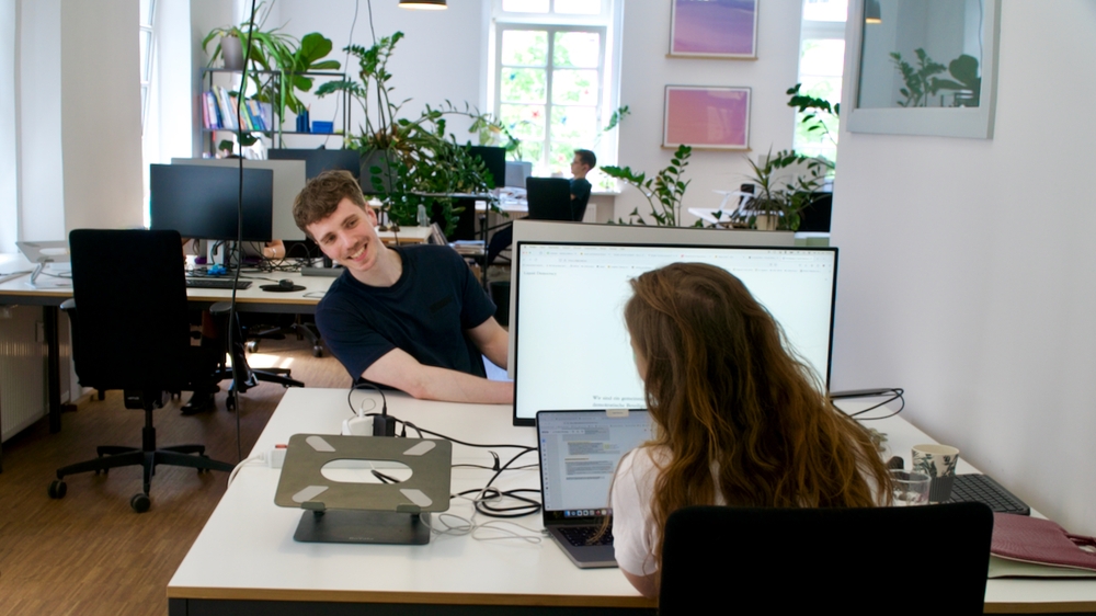 The Picture shows two persons who sit at a desk and smile at each other.