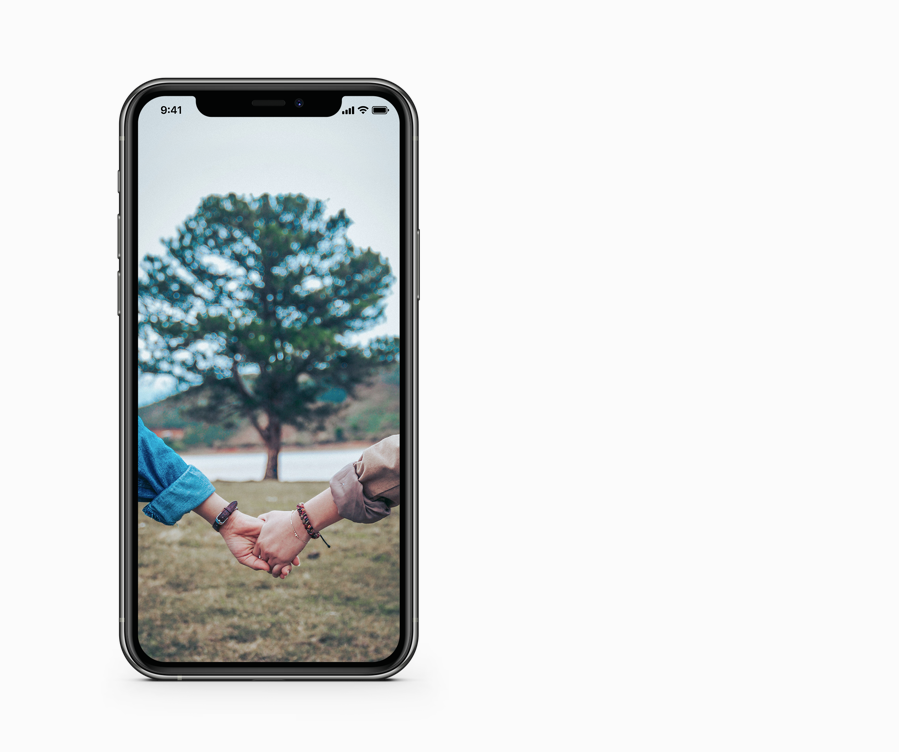 Auf einem Smartphonebildschirm ist das Foto von zwei sich halten Händen unter einem mittig im Hintergrund verschwommen zu sehenden Baum abgebildet.