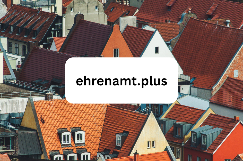 Roofscape with various gables and roofs in different shapes and colors topped by a white rectangle with the text 'ehrenamt.plus'