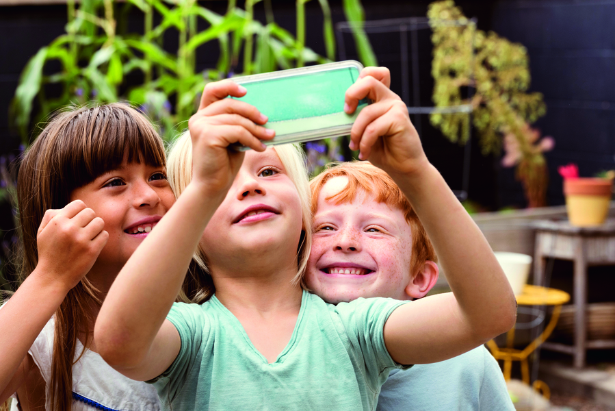 Auf dem Bild sind drei lachende Kinder zu sehen, die ein Smartphone in der Hand halten und betrachten.
