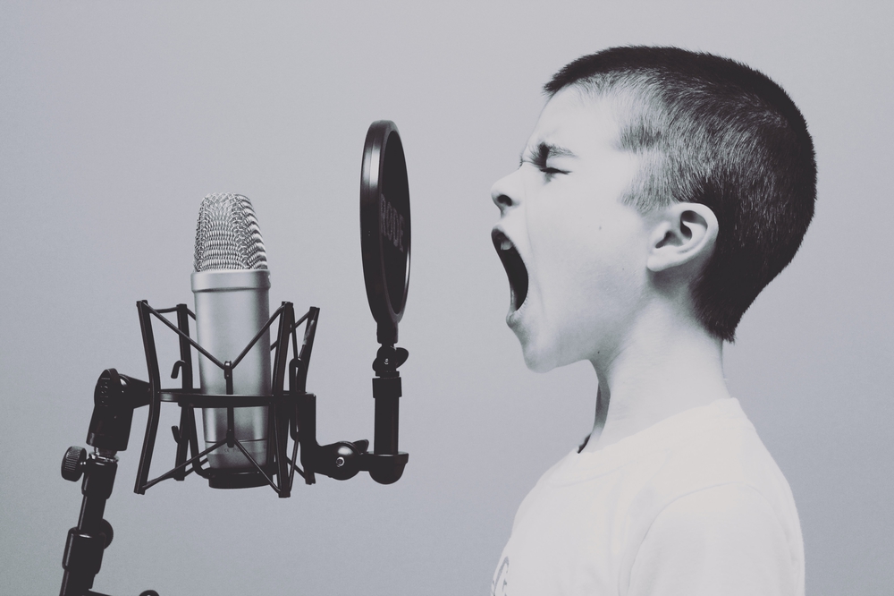 Auf dem Bild ist ein Kind zu sehen, dass in ein Mikrofon schreit. Das Bild ist in schwarz weiß gehalten.