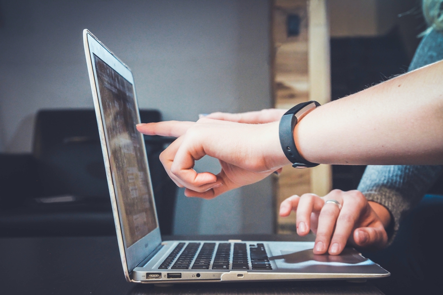 Auf dem Bild sind die Hände von zwei Personen zu sehen, die auf einen Laptop benutzen und auf dessen Bildschirm zeigen.