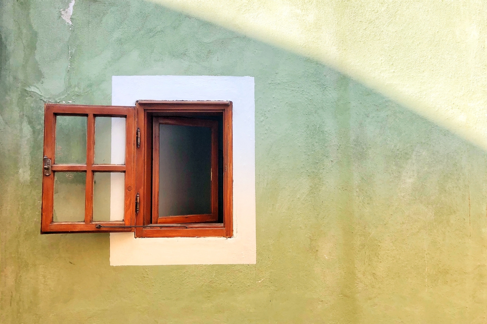 Auf dem Bild ist eine grüne Hauswand mit einem kleinen geöffneten Fenster auf der linkes Seite zu sehen.
